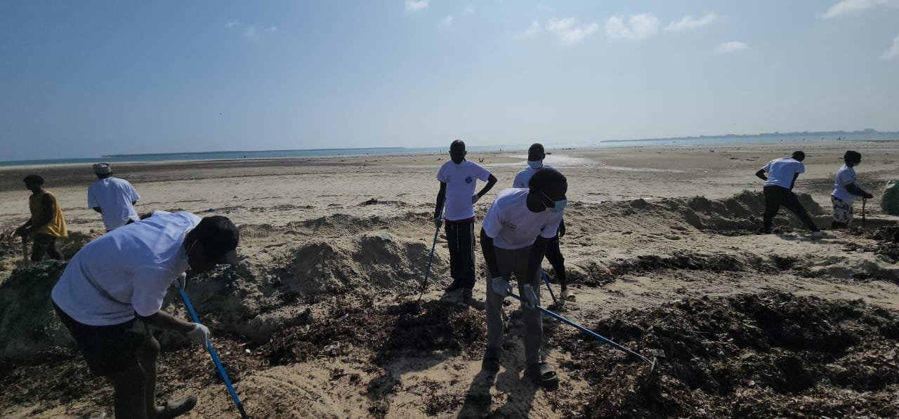 Volunteers raking the beach at Mbezi Beach A with ocean behind