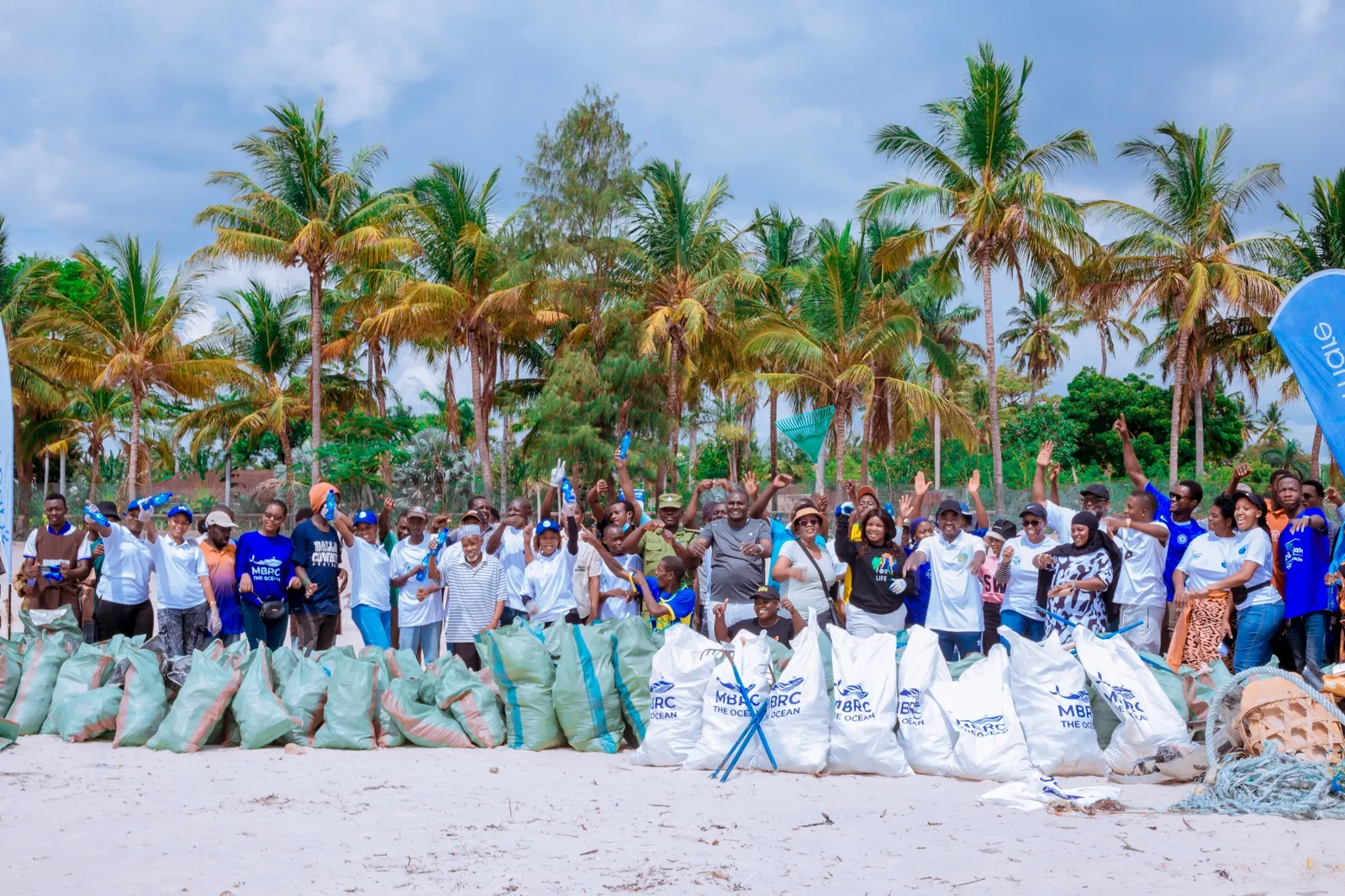 JMMBA community beach clean-up with coconut trees and shoreline backdrop